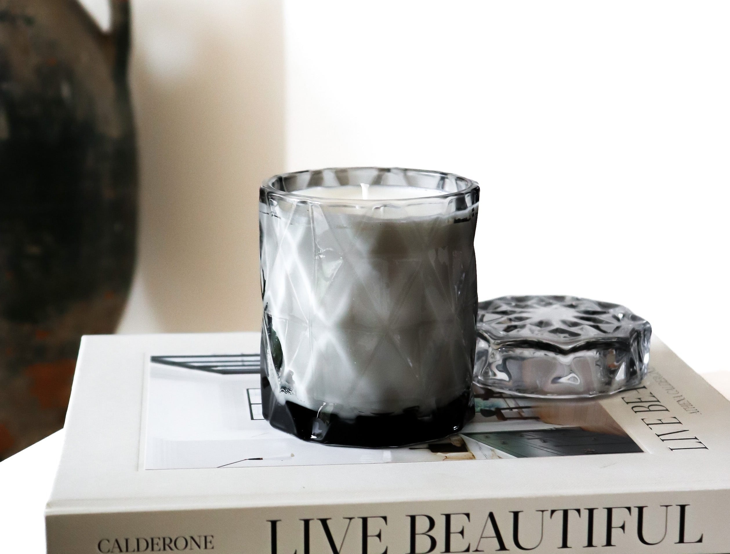 coconut wax candles in a gray glass jar with lid on stacked coffee table books