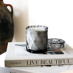 coconut wax candles in a gray glass jar with lid on stacked coffee table books