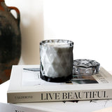 coconut wax candles in a gray glass jar with lid on stacked coffee table books