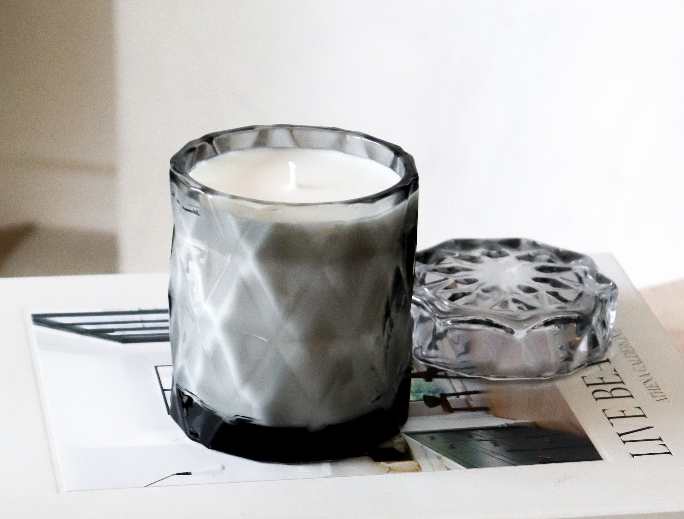 coconut wax candles in a gray glass jar with lid on stacked coffee table books