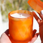 coconut wax candle in matte orange glass jar with lid in outside garden