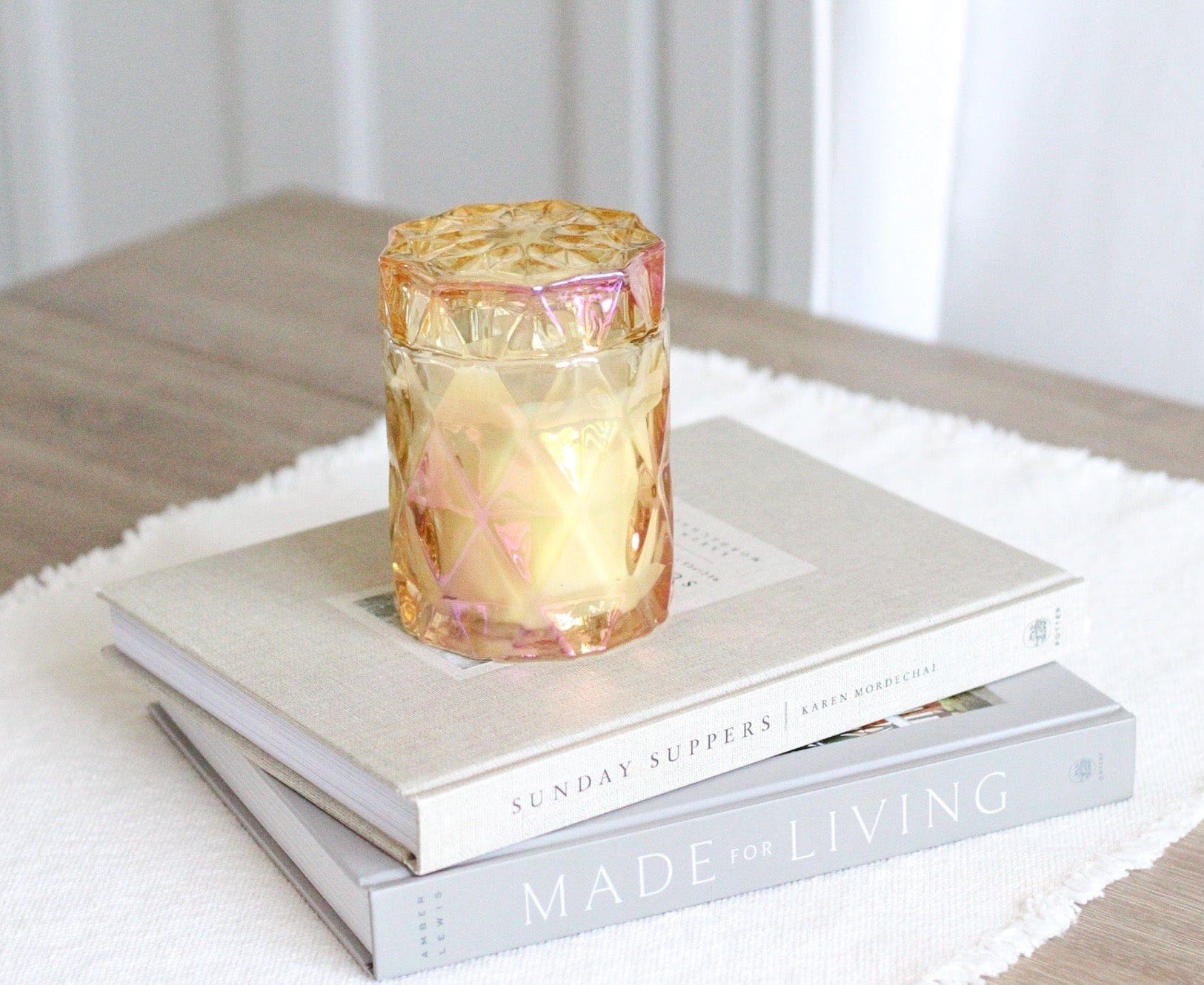coconut wax candles in iridescent glass jar with lid on stack of coffee table books