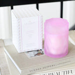 lavender lilac color glass candle jar with lid next to candle packaging box on stack of books