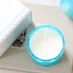 double wick coconut wax candle in light teal color glass jar on stack of coffee table books