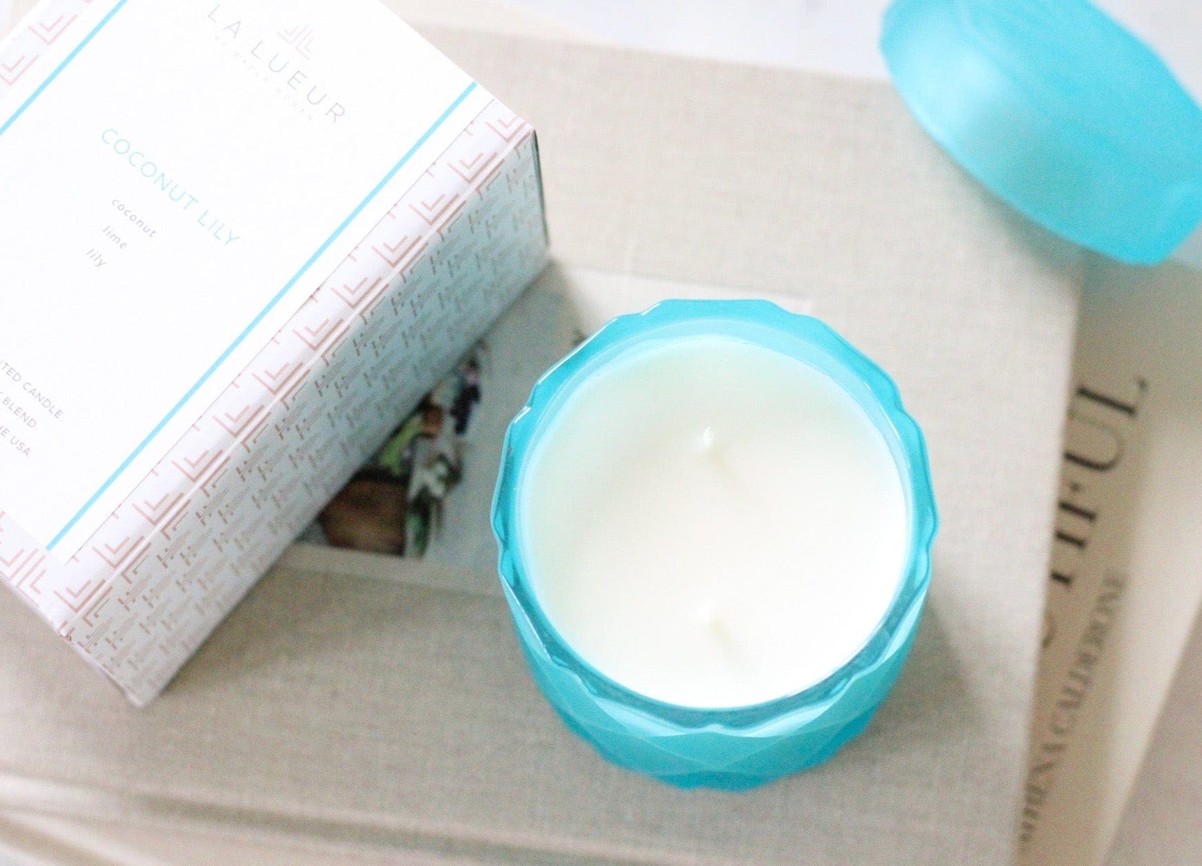 double wick coconut wax candle in light teal color glass jar on stack of coffee table books