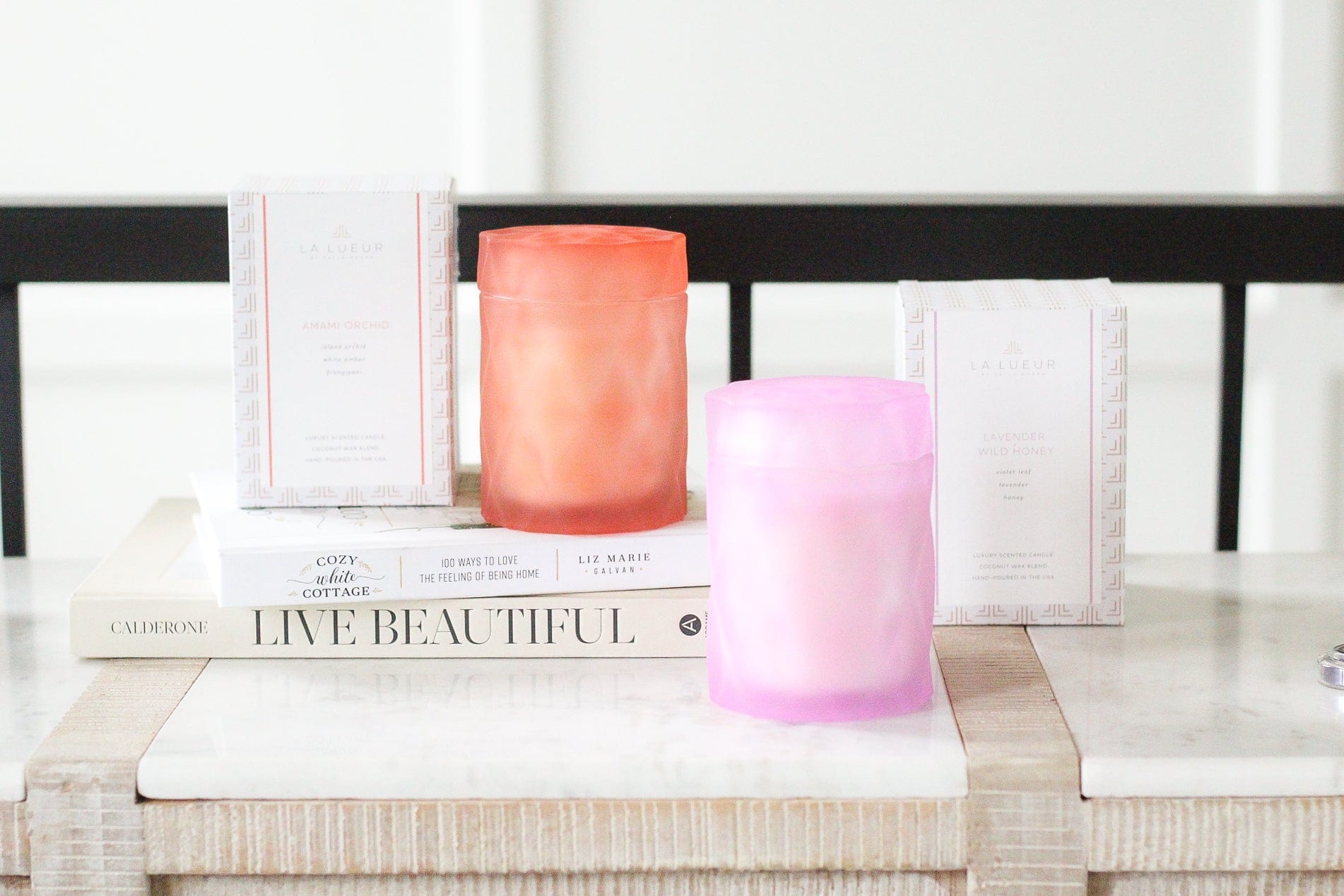 lavender lilac color and coral color glass candle jars with lids next to candle packaging on coffee table books